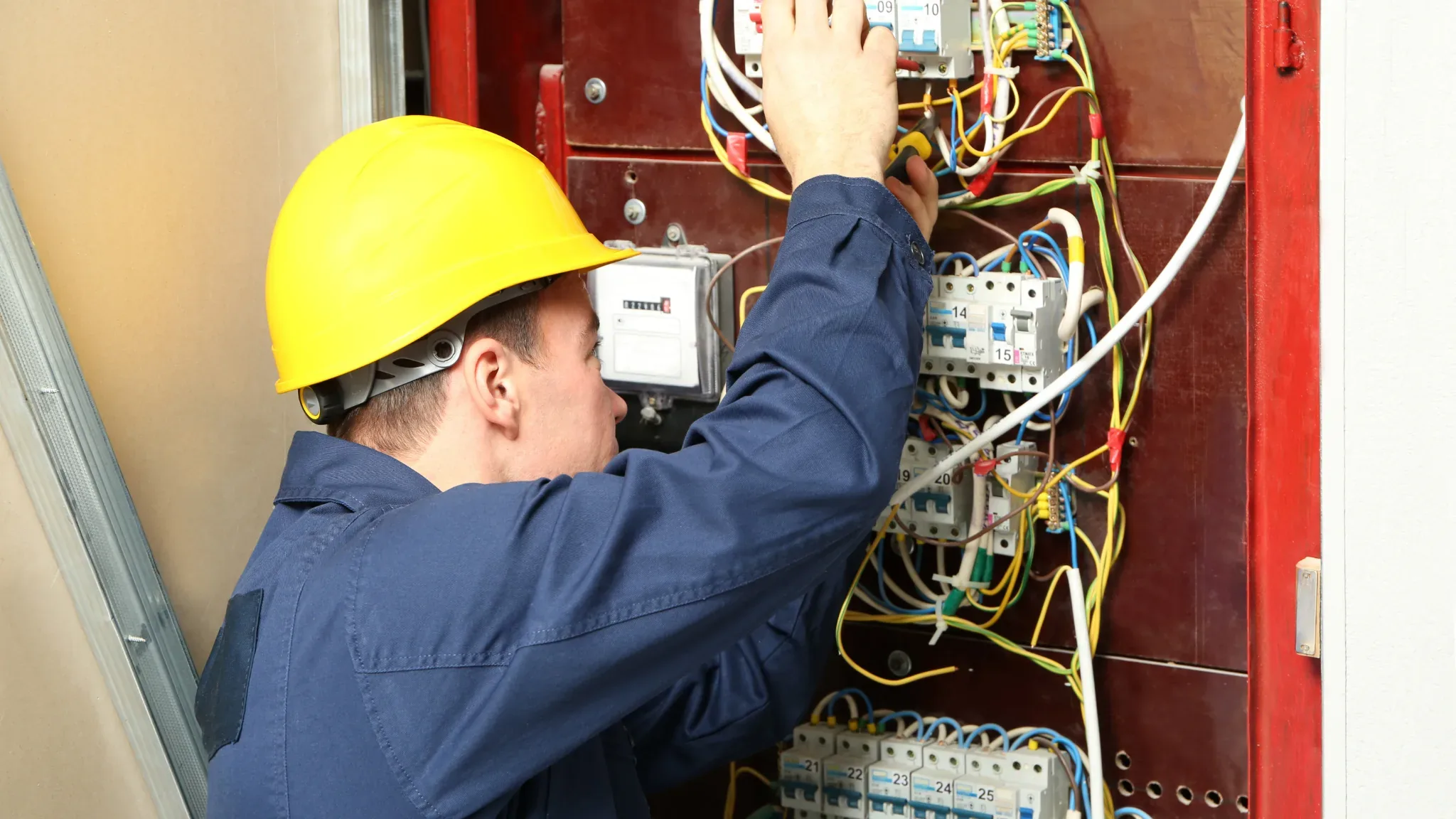 Licensed electrician in safety gear working on a residential electrical panel with circuit breakers and wiring